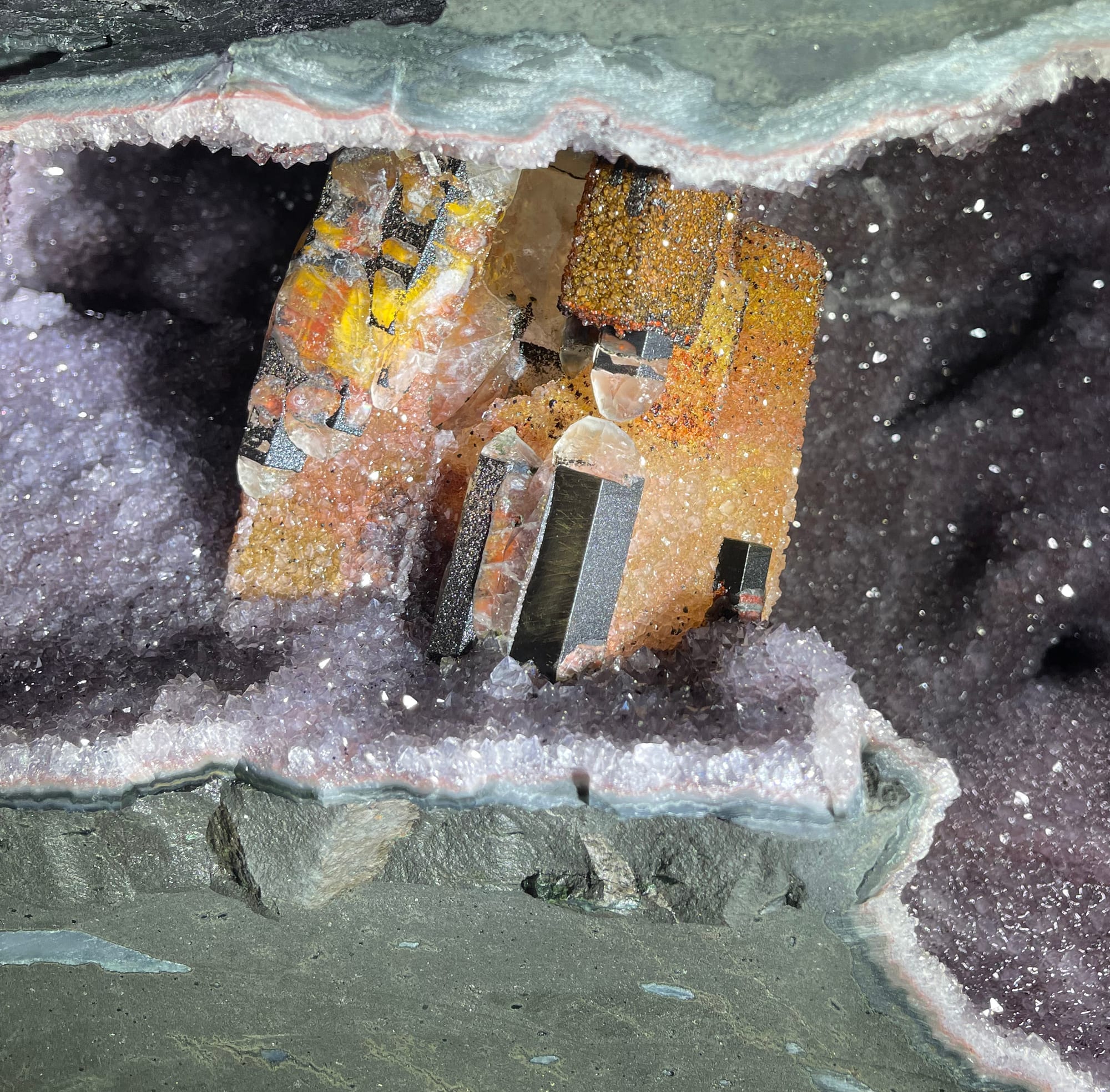 Geoda grande abierta con cristales de calcita naranja dentro; arriba, unos guantes de trabajo