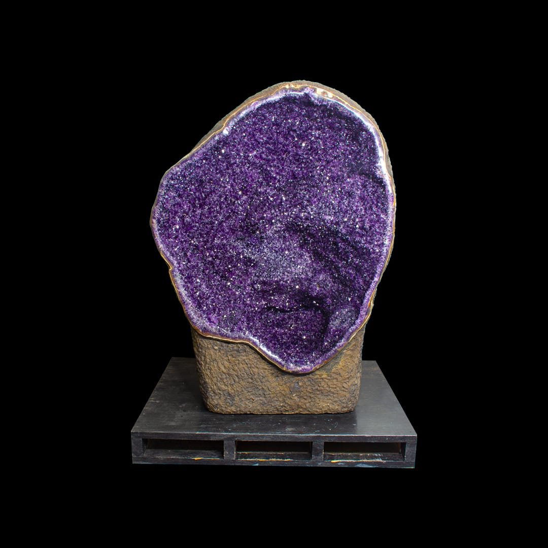 An open amethyst geode on its own rock, on a metal base