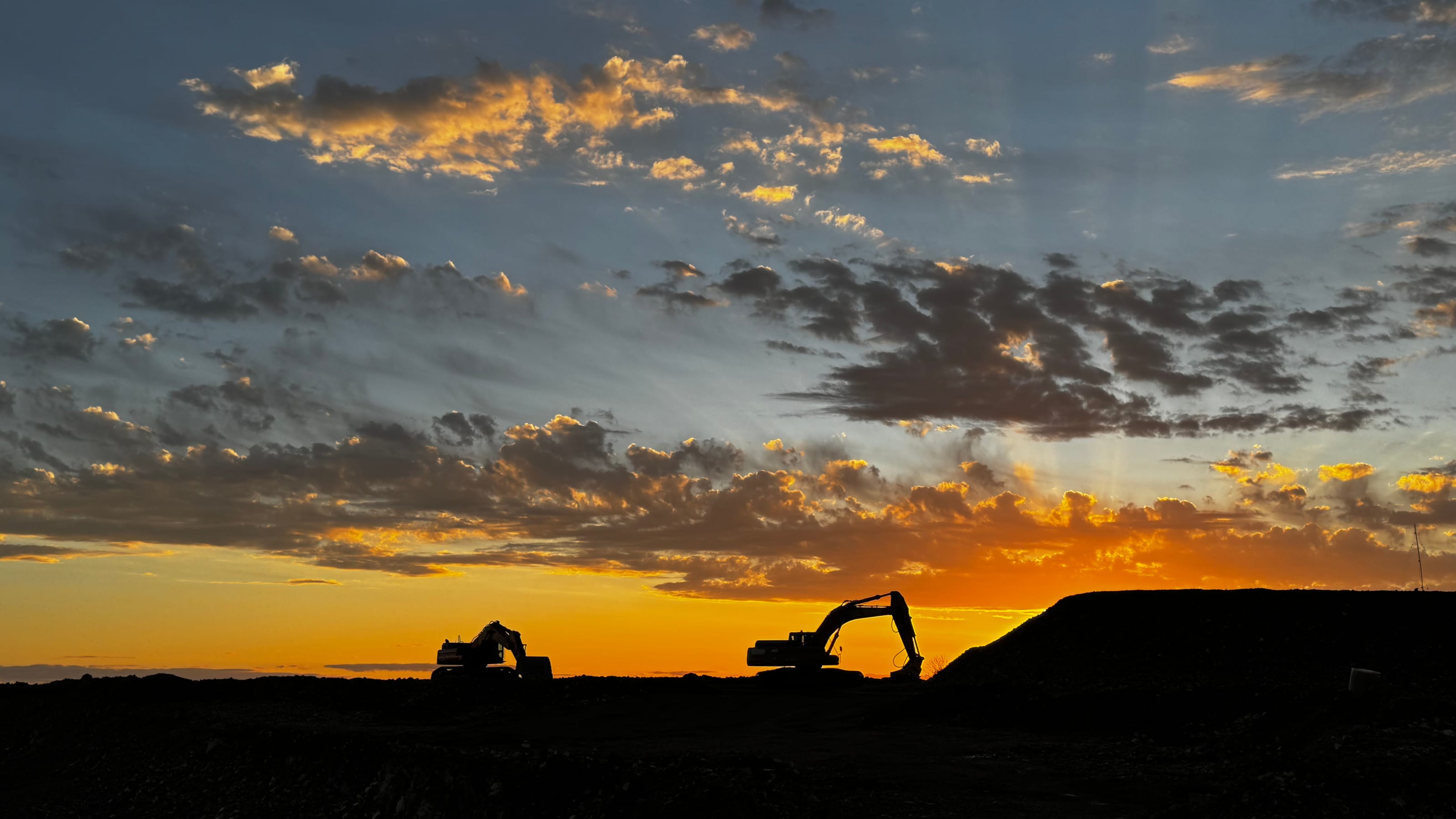 Sunset over a quarry in Los Catalanes, with two machines silhouetted against the sky