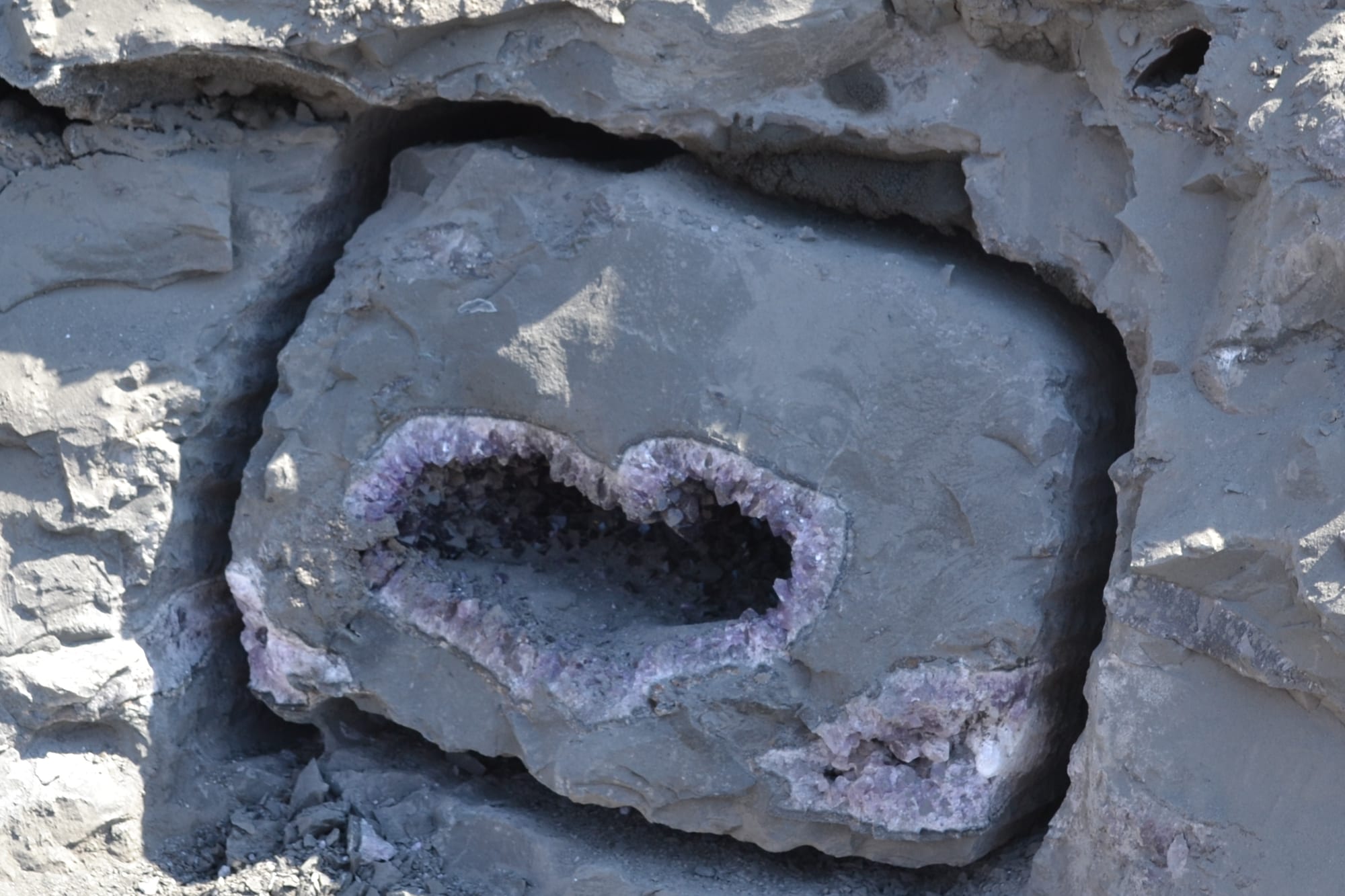 Geoda de amatista todavía encastrada en la roca del frente de cantera: el bloque recortado y la cavidad abierta, antes de extraerla