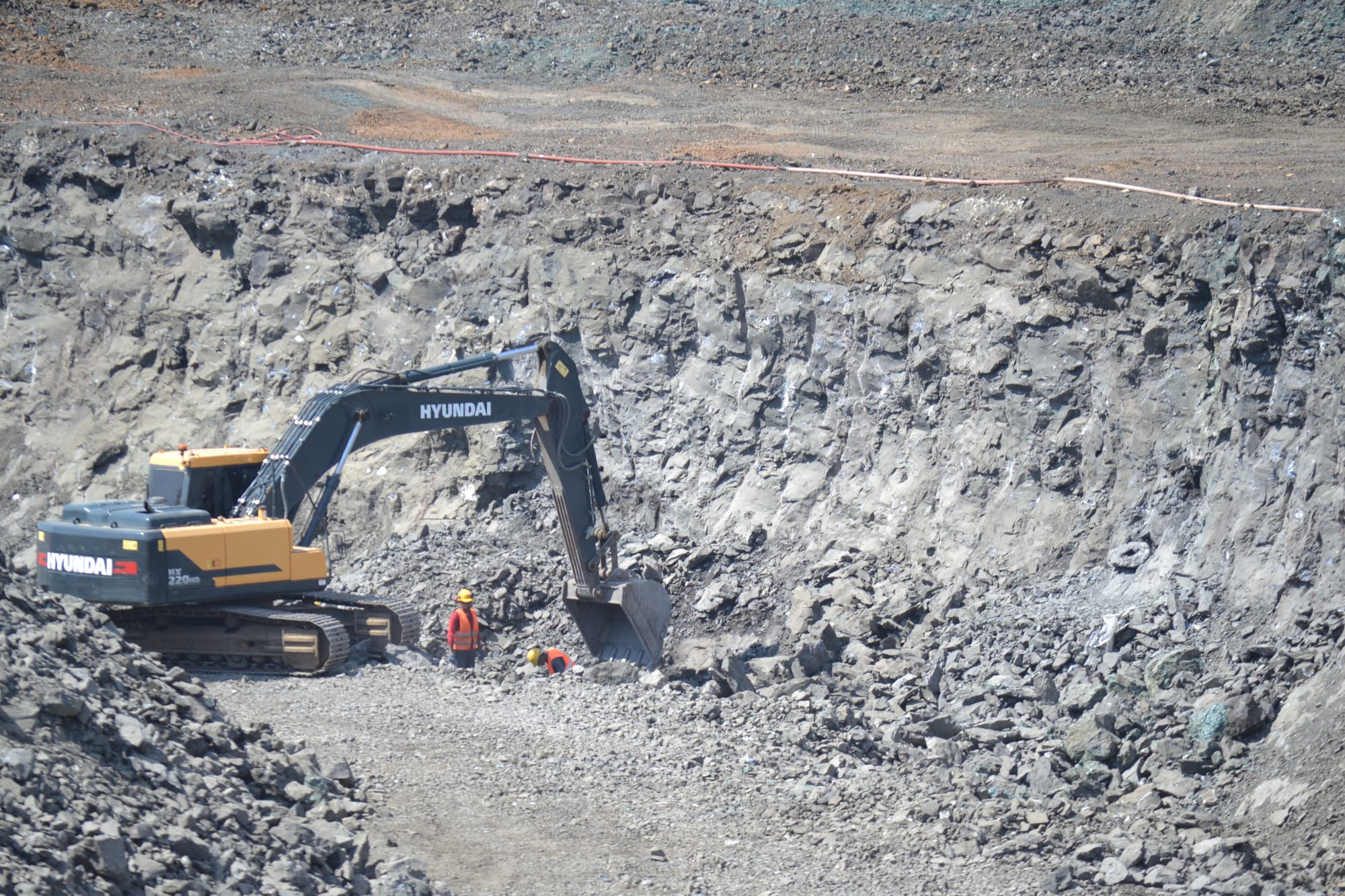 Frente de basalto de la cantera, con una excavadora y dos operarios al pie de la pared