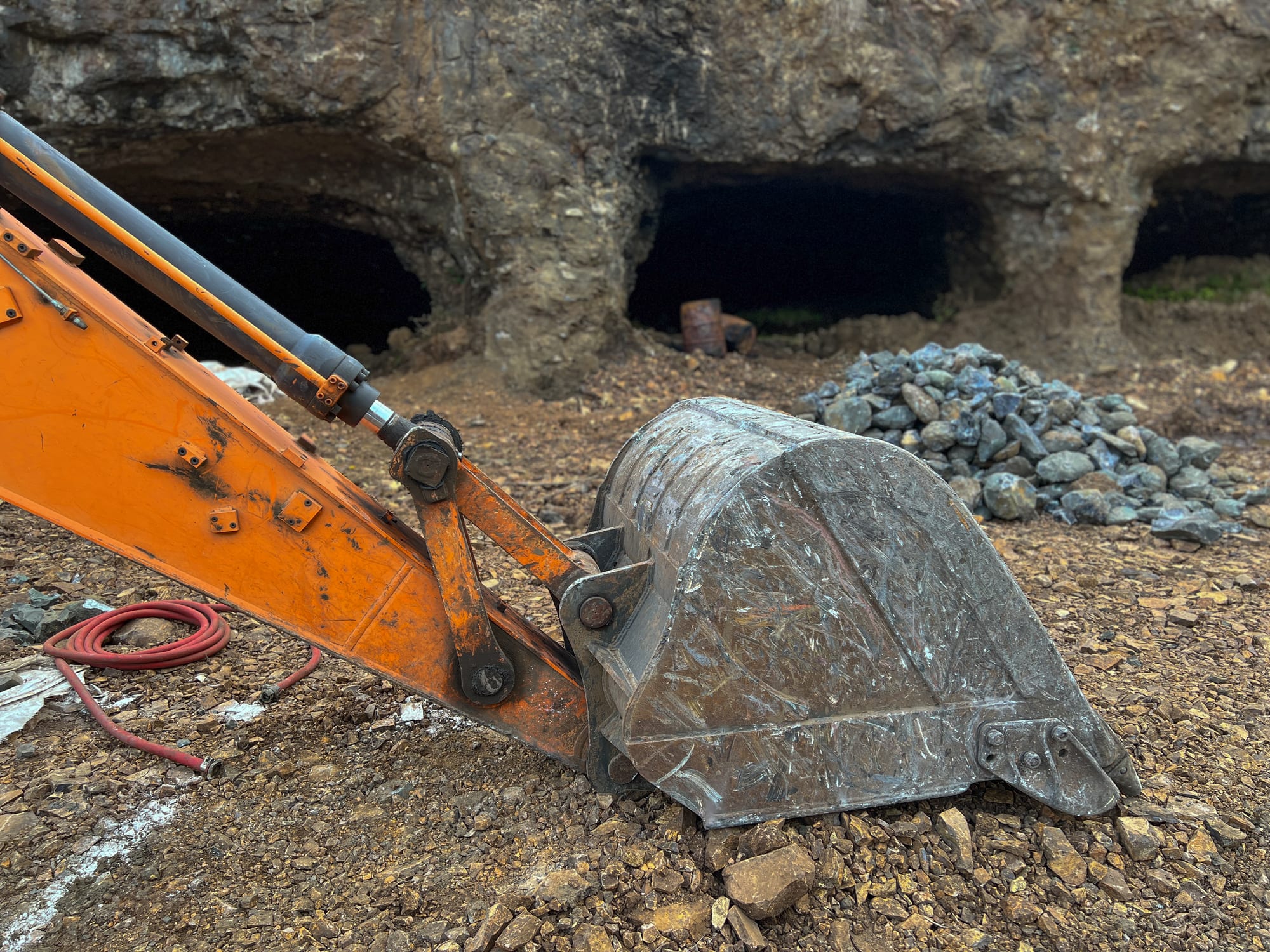 Gallery entrances in the rock face, with an excavator bucket in the foreground