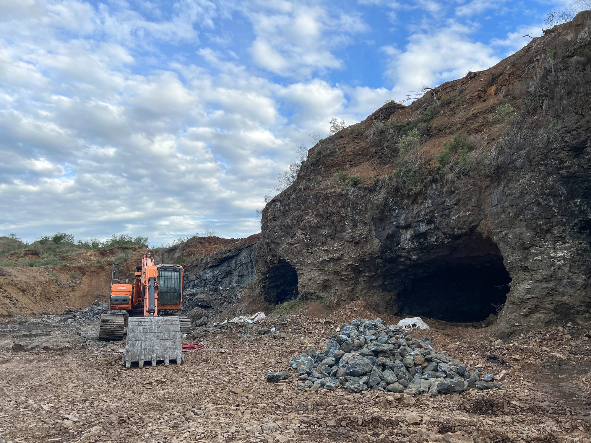 An excavator beside the gallery entrances cut into the rock face